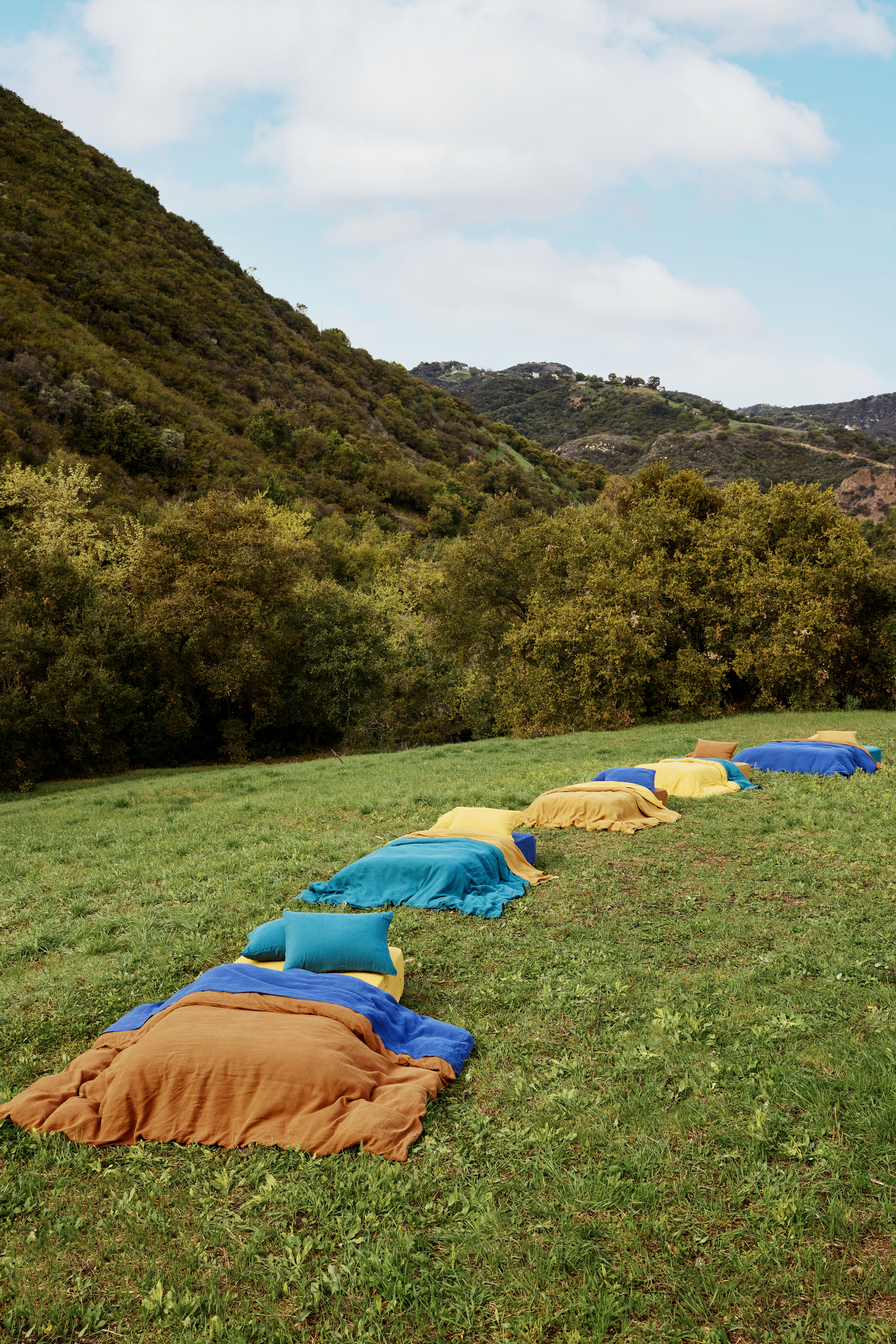 made beds in a row with colorful bedding, standing on grass in a lush, hilly setting