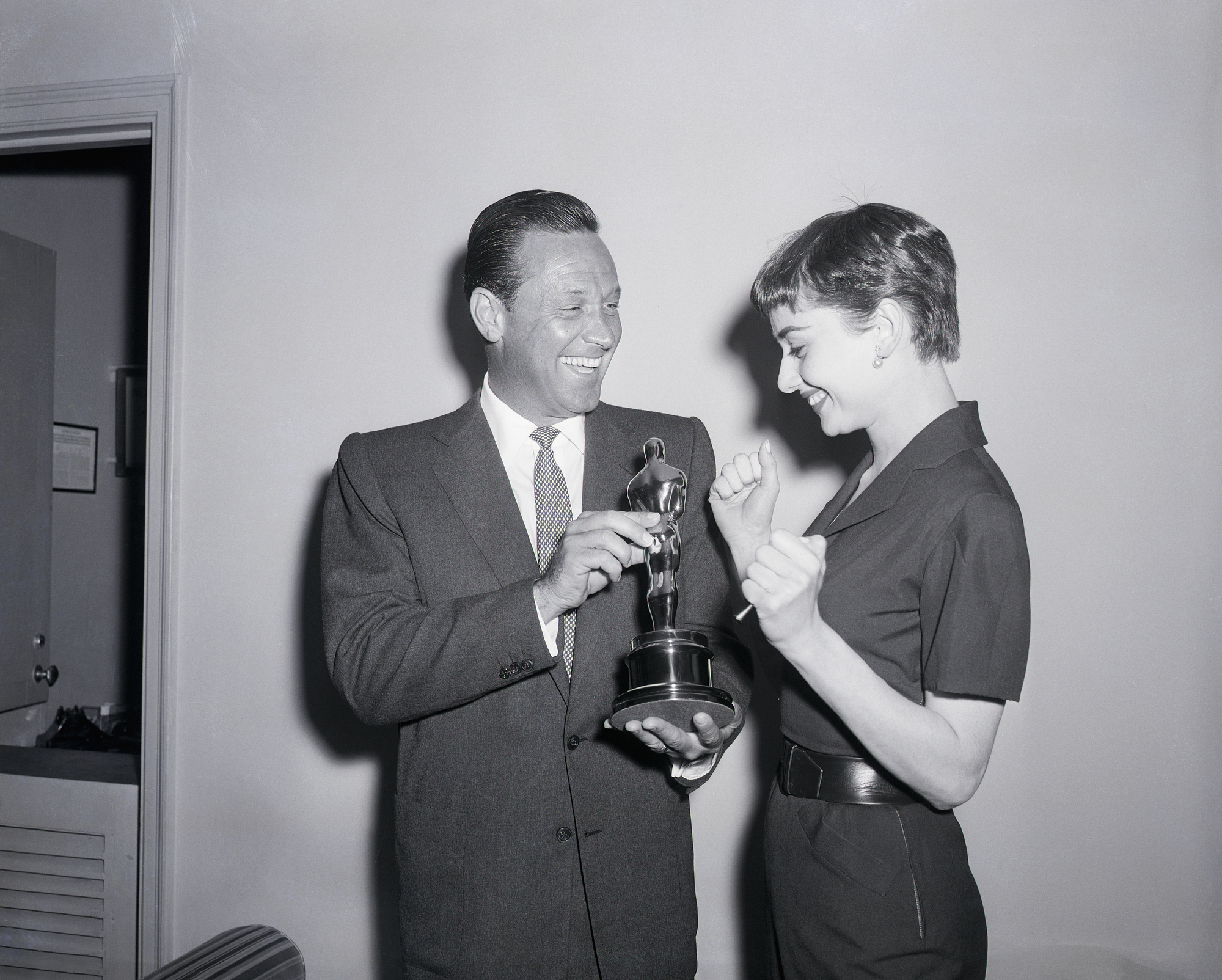 Stage and screen actress Audrey Hepburn, who won Hollywood's Academy Award weeks ago for her performance in the film "Roman Holiday," is ecstatic with delight after finally receiving the "Oscar" with her name on it, 5/3, at a special ceremony in Manhattan's Hotel Pierre. Sharing her enthusiasm is fellow "Oscar" winner William Holden, who picked up a gold statuette for his performance in "Stalag 17." The two are co-starring in the forthcoming cinema, "Sabrina," a Paramount picture.